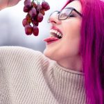 femme en pull gris tenant des fruits ronds rouges