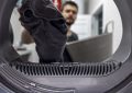 Homme chargeant un lave-linge, illustrant le sujet « Pièces détachées de lave-linge : réparer ou remplacer ? Les signes clés ».