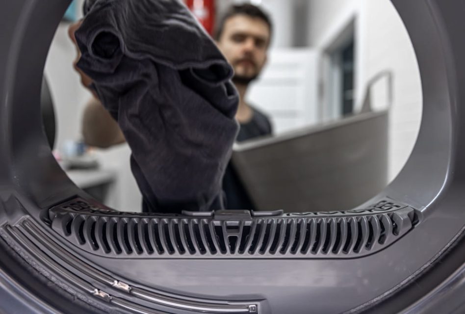 Homme chargeant un lave-linge, illustrant le sujet « Pièces détachées de lave-linge : réparer ou remplacer ? Les signes clés ».
