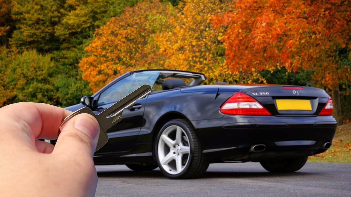 Une main tient des clés devant une voiture décapotable noire Une main tient des clés devant une voiture décapotable noire
